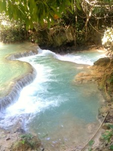 Blaugrünes Wasser fließt über mehrere Natursteinbecken ins Tal